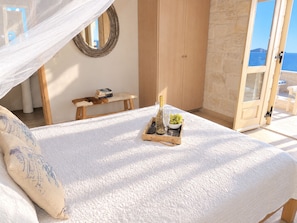 Une chambre à coucher comprenant un lit, une table de chevet, un miroir, une armoire en bois et un balcon avec vue sur la mer.
