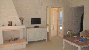 Une pièce avec un mur en pierre, une cheminée, un téléviseur, un meuble en bois et une table sur laquelle se trouve un saladier rempli de fruits.