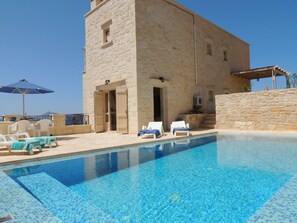 A stone building with a pool, lounge chairs, and an umbrella.