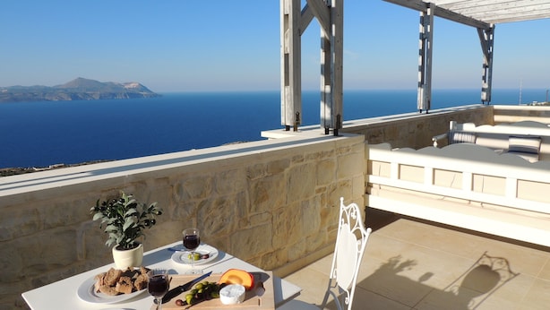 Une terrasse avec une table dressée pour un repas, une vue sur la mer et un mur en pierre.