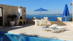 Un espace aménagé au bord de la piscine, avec vue sur la mer, des murs en pierre et du mobilier d’extérieur.