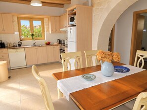 A kitchen with wooden cabinets, a dishwasher, and a dining area with a table set for two. - A charming 3 bedroom stone villa w/ privacy, private pool & fantastic sea views. (Chania)