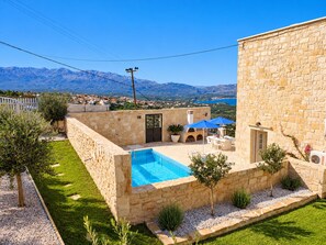 A stone building with a swimming pool, outdoor seating, and a view of mountains. - A charming 3 bedroom stone villa w/ privacy, private pool & fantastic sea views. (Chania)