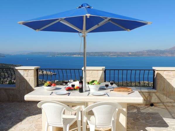 A table with a blue umbrella, white chairs, and a view of the sea.