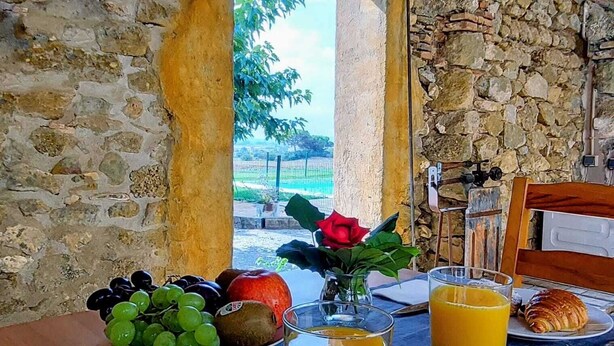 A breakfast table with croissants, fruit, and juice, set against a stone wall with a view of greenery. - Rural house for groups and hikers, nature and tranquility lovers. (La Torre Vella)