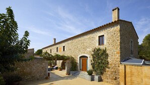 A stone building with a tiled roof, a wooden door, and a small window. There are potted plants and a bench outside. - Rural house for groups and hikers, nature and tranquility lovers. (La Torre Vella)