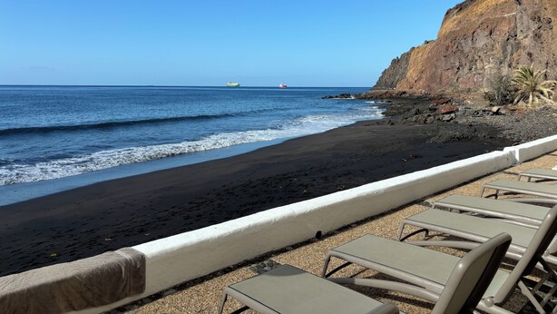 A beach with lounge chairs and a rocky cliff.