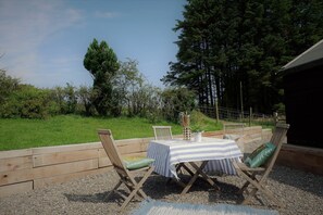 Un espacio al aire libre con mesas y sillas, rodeado por una terraza de madera y un campo cubierto de césped.