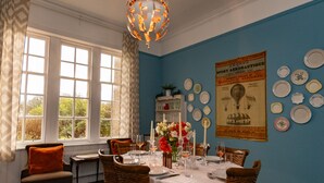 Une salle à manger avec une table dressée pour quatre personnes, un lustre et un mur orné d’assiettes et d’une affiche ancienne.