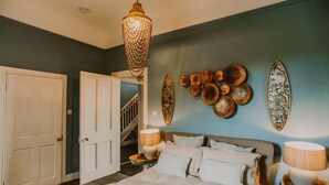 Une chambre à coucher avec un lit, des lampes de chevet, un lustre et des œuvres d’art décoratives au mur.