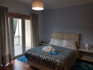 A hotel room with a large bed, a nightstand, a lamp, and a view of the outdoors.