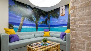 A room with a light blue sofa, yellow and purple cushions, a wooden coffee table with a plant, and a mural of a beach scene. - Petra design apartment Dubrovnik; FREE wireless internet and breakfast! (Dubrovnik)