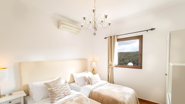 A bedroom with two beds, a chandelier, a window with a view, and a nightstand with a lamp. - Cortijo el Chenil rural retreat, La Perrita (Casarabonela)