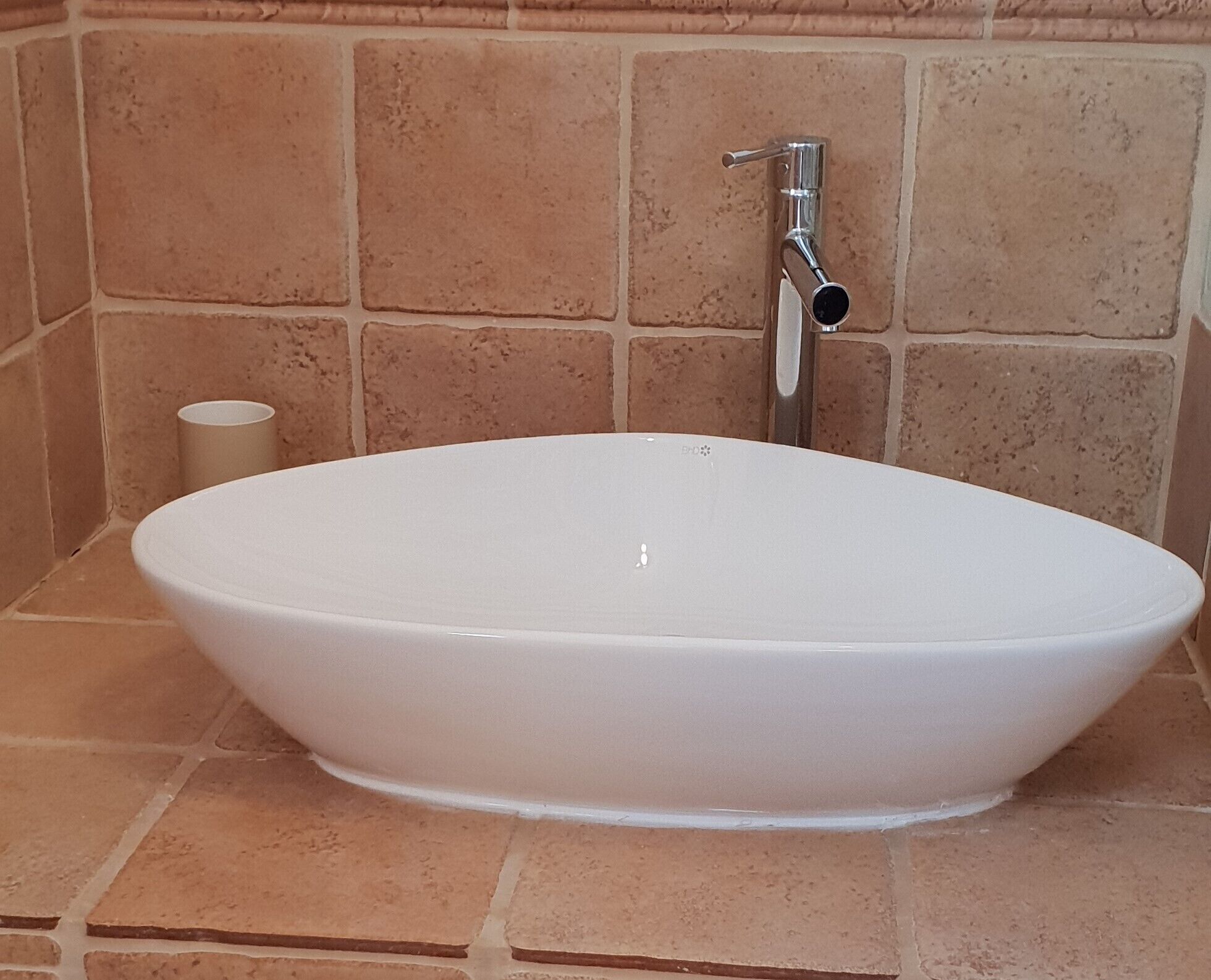 A white oval-shaped bathtub in a bathroom with beige tiled walls and a single white toilet paper roll.