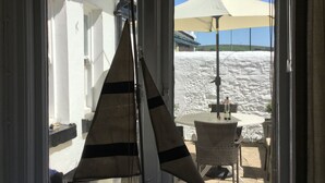 A sailboat model on a windowsill, a table with chairs, and a stone wall outside. - TRINITY COTTAGE. Charming historic cottage just off the Quay in Appledore. (Appledore)