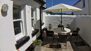 A patio with a round table and chairs, a white umbrella, and potted plants. - TRINITY COTTAGE. Charming historic cottage just off the Quay in Appledore. (Appledore)