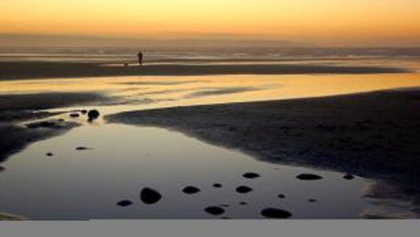 A beach scene with a person walking on the sand, a calm sea, and a sunset sky. - TRINITY COTTAGE. Charming historic cottage just off the Quay in Appledore. (Appledore)