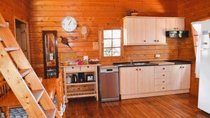 Interior de uma cabana de madeira, com área de cozinha, incluindo armários de madeira, pia, fogão e lava-louças.