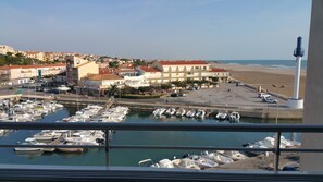 Una marina con barcos amarrados, una playa y edificios al fondo.