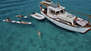 Ein großes Boot mit überdachter Deckfläche, einer Kabine und einem Essbereich. Mehrere kleinere Boote und Personen sind im Wasser darum verteilt.