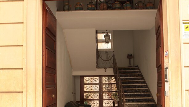 A staircase leading to a room with a tiled floor, a wooden chair, and a cabinet with glass doors.
