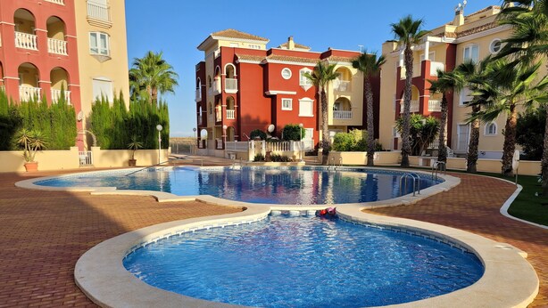 Un área de piscina con dos piscinas, rodeada de palmeras y un edificio con balcones.
