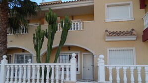 Un edificio de dos pisos con fachada color beige, balcones blancos y un portón blanco.