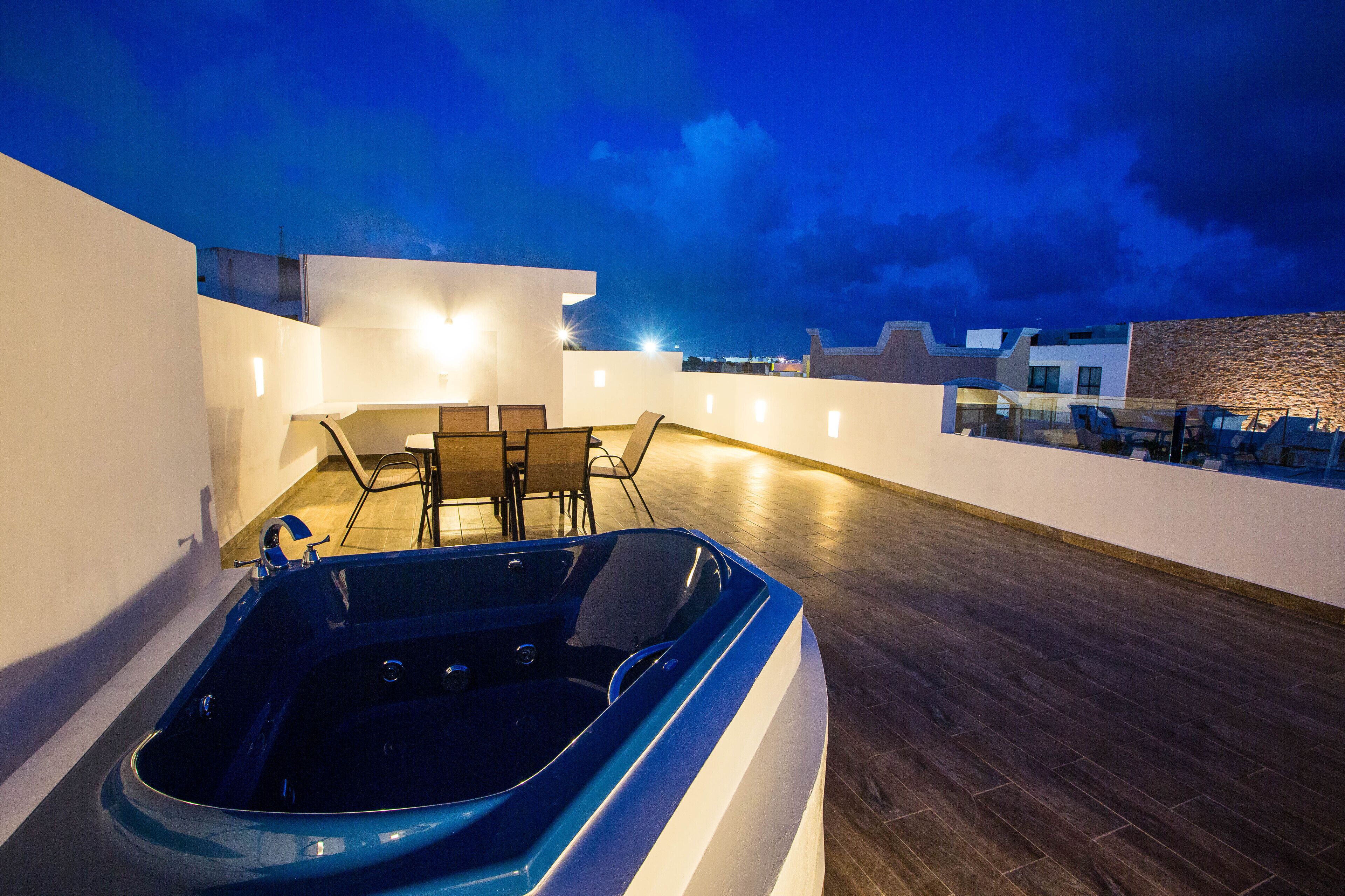 Eine Dachterrasse mit Whirlpool, Sitzgelegenheit und Blick auf die Stadt bei Dämmerung.