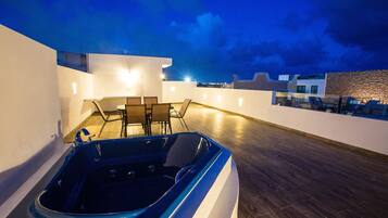 Eine Dachterrasse mit Whirlpool, Sitzgelegenheit und Blick auf die Stadt bei Dämmerung.