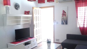 Un salon avec un téléviseur posé sur un meuble blanc, un canapé, une table basse et une porte donnant sur l’extérieur.
