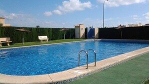 Une piscine avec un bord carrelé, un banc et un petit bâtiment en arrière-plan.