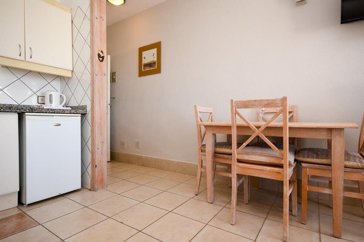 A compact kitchen with a refrigerator, a coffee maker, and a wooden dining table with chairs.
