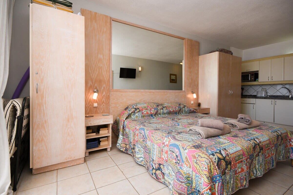 Een slaapkamer met een bed, een grote spiegel, een televisie en een kitchenette.