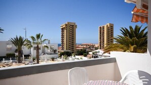 En balkon med et bord og stole, der kigger ud over et kystområde med høje bygninger og palmer.