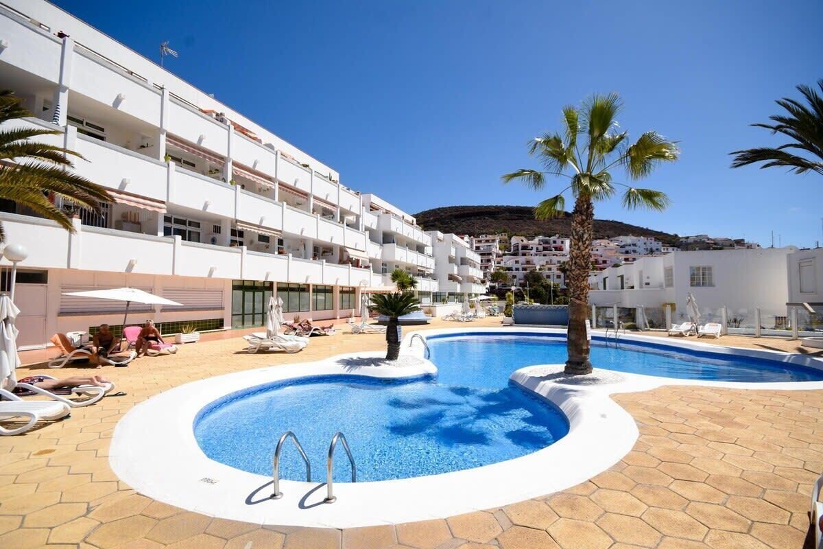 A hotel with a swimming pool, sun loungers, and palm trees.