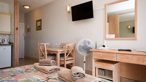 Et hotelværelse med seng, skrivebord, stol, fjernsyn, ventilator og et lille tekøkken.