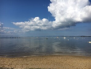 Una playa con aguas tranquilas, barcos y un puente a lo lejos.