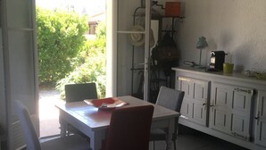A dining area with a table and chairs, a kitchen area with cabinets, and a view of greenery outside. - Very nice and cozy house 10 minutes from the Bassin   (Arès)
