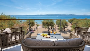 A balcony with wicker furniture, a table with a fruit platter and drinks, and a view of the beach and sea.