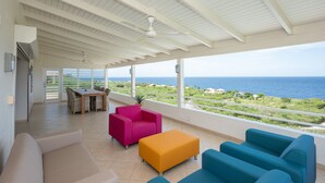 A spacious balcony with a view of the sea, furnished with a table, chairs, and colorful sofas. - Luxury Villa "Lions Cliff" with fantastic views over the Caribbean Sea (St. Willibrordus)