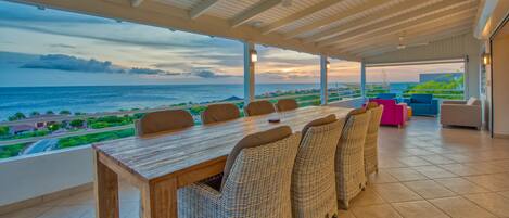 A dining area with a view of the ocean, a covered patio, and outdoor seating.