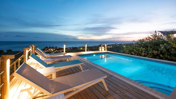 A pool with lounge chairs and a wooden deck, overlooking a coastal area. - Luxury Villa "Lions Cliff" with fantastic views over the Caribbean Sea (St. Willibrordus)