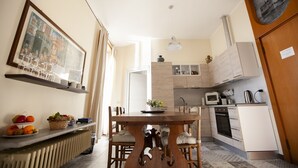 Una cocina moderna con armarios blancos, horno empotrado y microondas. Hay una mesa de comedor con sillas y una cesta de frutas en la encimera.