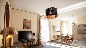 Habitación de hotel con televisor, lámpara, ventilador, mesa de comedor y zona de cocina.