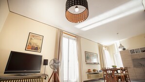Una sala de estar con televisión, ventilador, mesa de comedor con sillas y zona de cocina.
