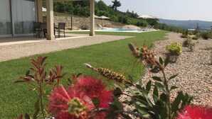 Et overdækket udendørsområde med pool, stensætning og grøn vegetation.