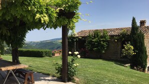 Un patio con tavolo e panche in legno, circondato da un prato curato e un edificio in pietra con tetto in tegole.