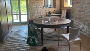 Una stanza rustica con pareti in pietra, un tavolo rotondo in legno, sedie e una borsa in tela verde.