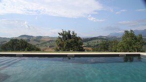 Una piscina trasparente con vista su dolci colline e montagne lontane.