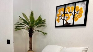 A bed with a white bedspread and a patterned throw, a single white pillow, a small potted plant, and a framed picture of a tree on the wall. - Room in the heart of Cancun (29)